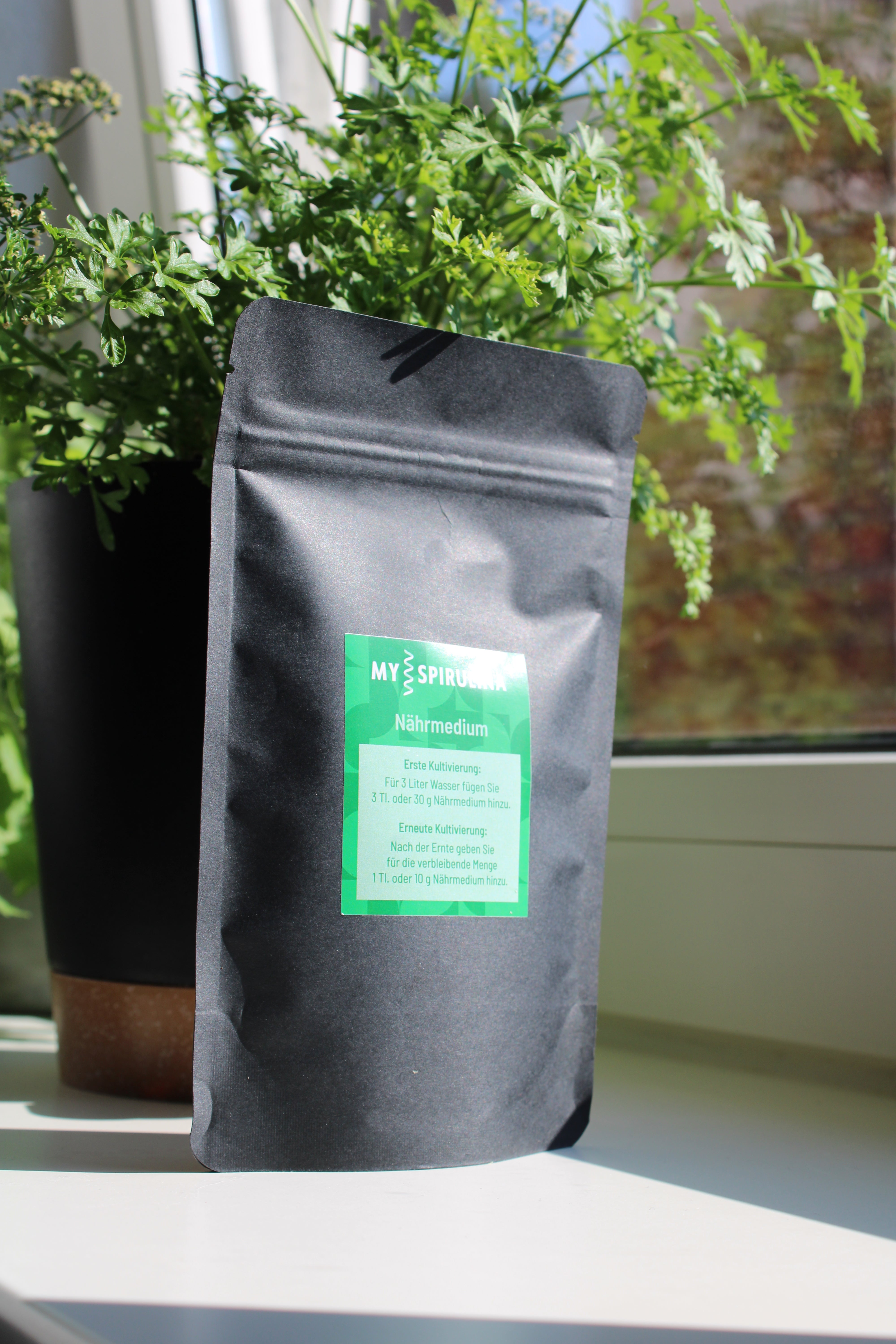 Rückseite der schwarzen Spirulina-Verpackung mit detaillierter Anleitung zur Kultivierung: Text und grafische Symbole erklären die Schritte zur Herstellung von Spirulina, klar und übersichtlich dargestellt.