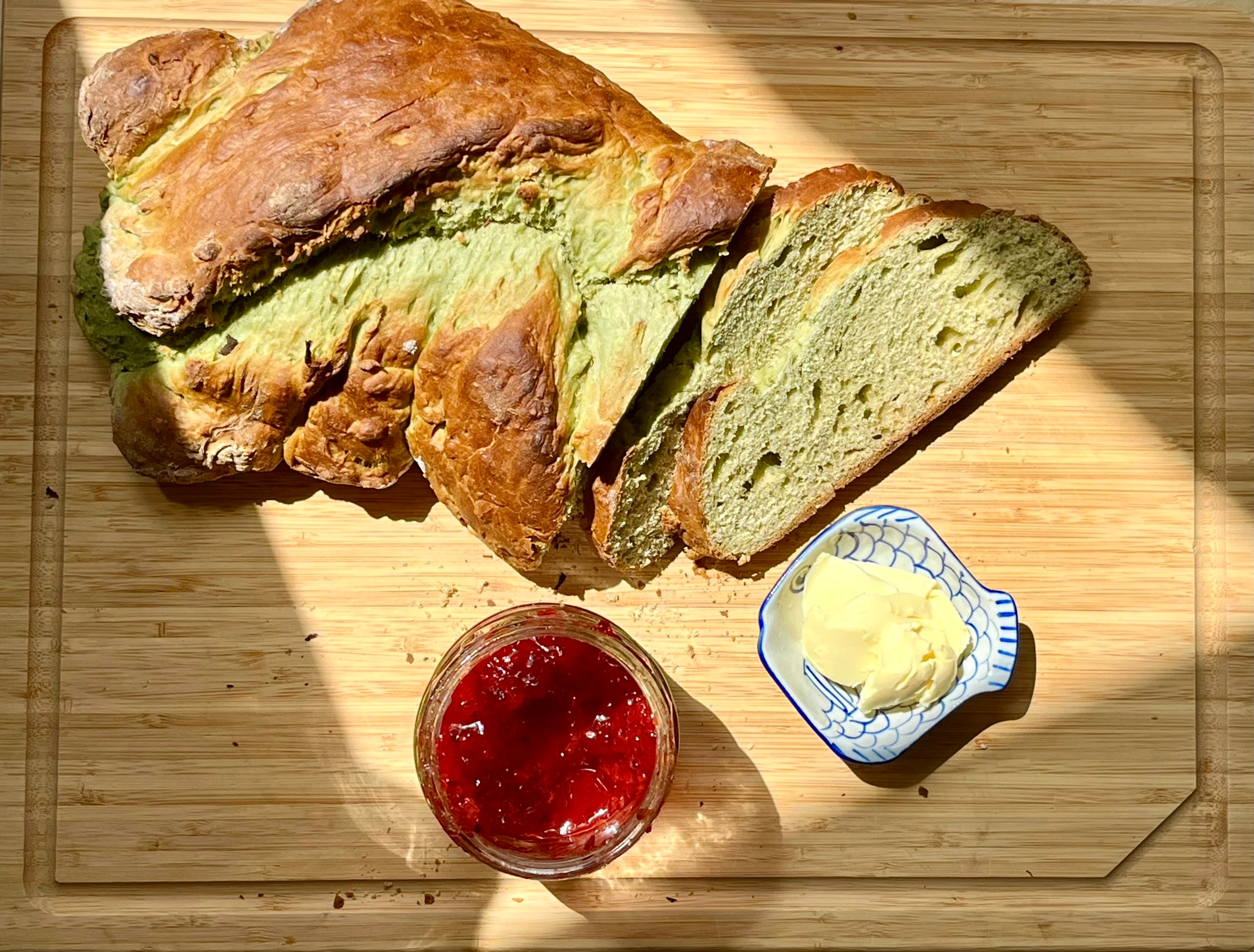 Hefezopf auf einem Holzbrettchen, serviert mit Marmelade und Butter in kleinen Portionen daneben.