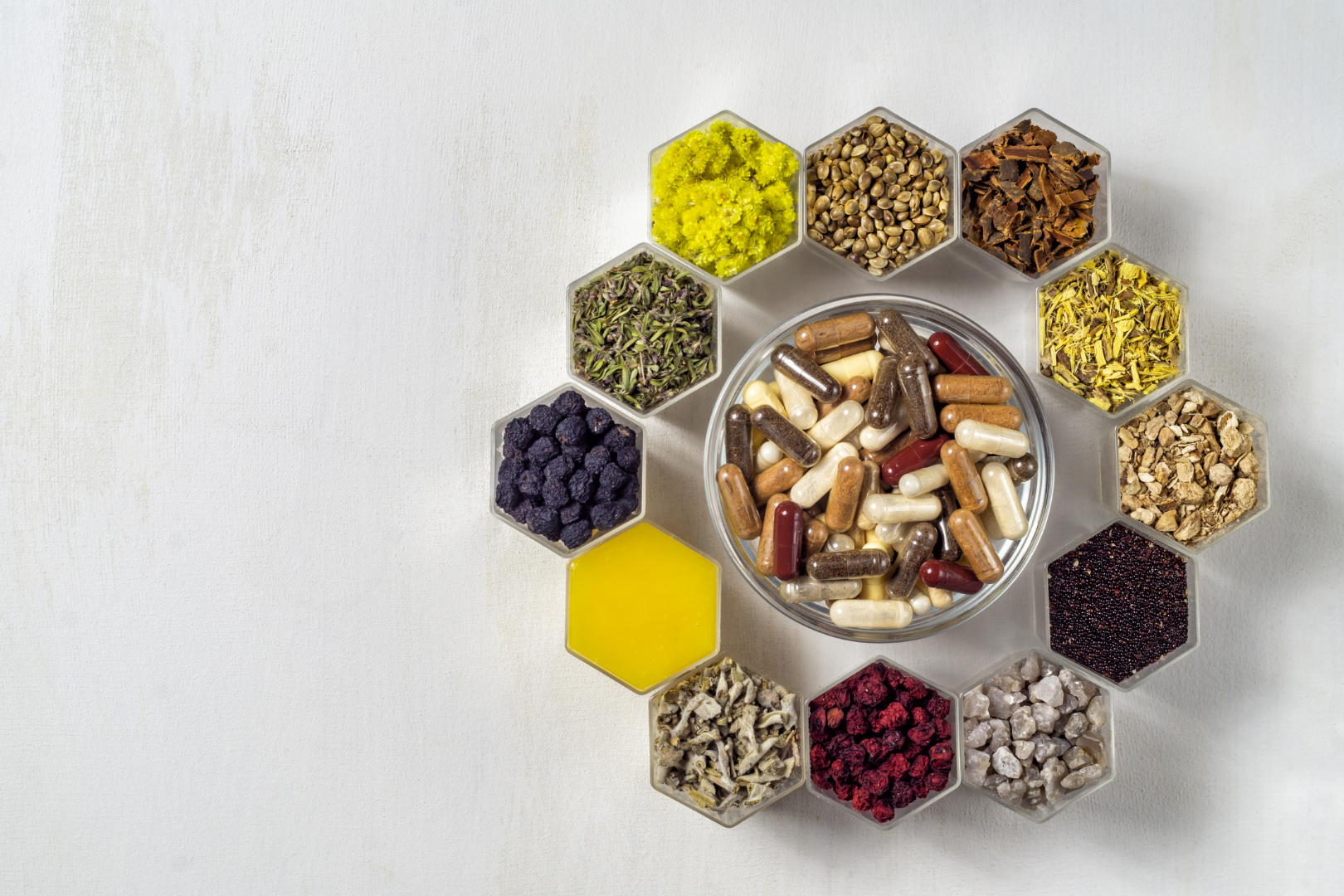 Mehrere Schüsseln mit verschiedenen Mineralien in Pulver- oder Granulatform, arrangiert um eine größere Schüssel in der Mitte, die mit Kapseln gefüllt ist – als Darstellung von Mineralien in ihrer Rohform zur Nahrungsergänzung.