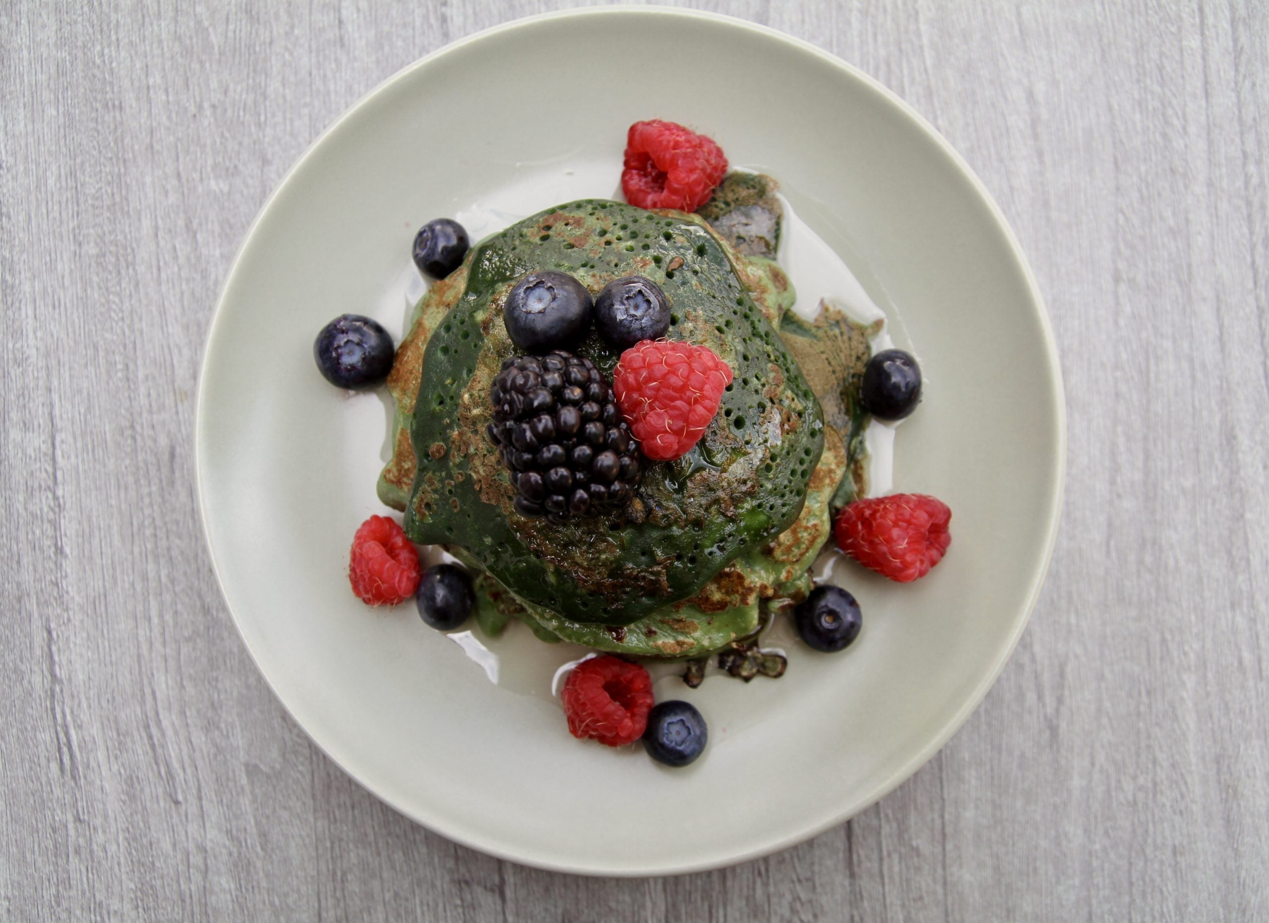 Pancakes mit Spirulina, die eine grünliche Farbe haben, garniert mit frischen Blaubeeren und Himbeeren.