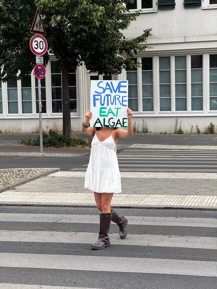 Person hält Schild „Save Future Eat Algae“ für nachhaltige Spirulina-Ernährung